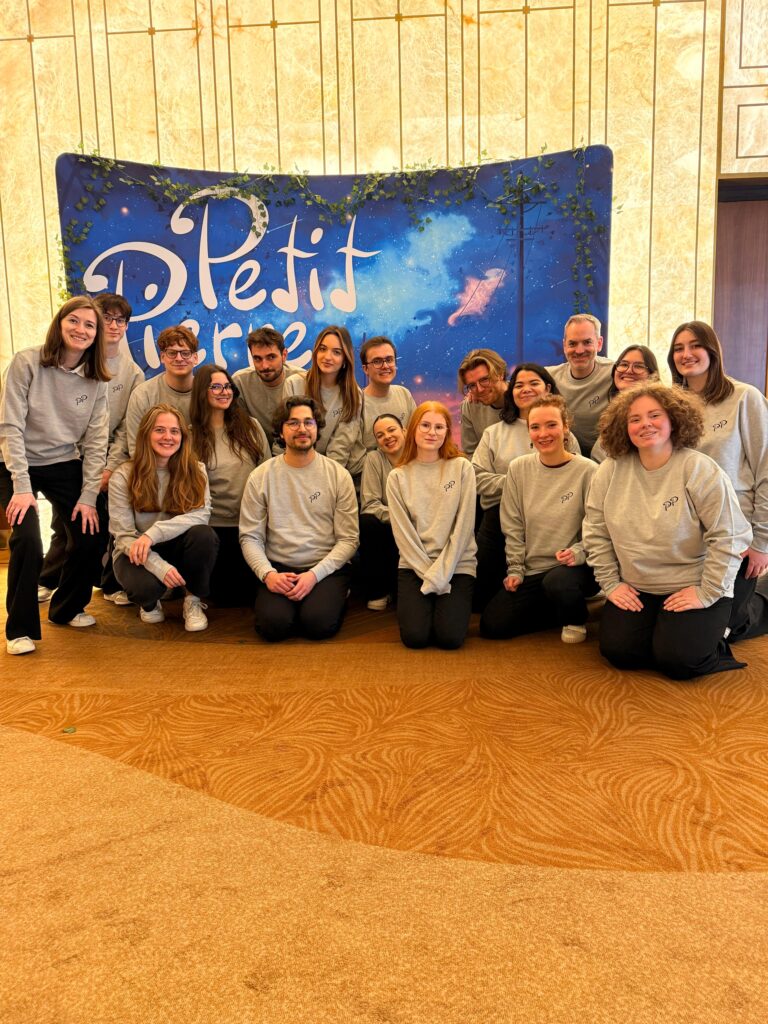 Photo de groupe des choristes d'Ineffable en sweat gris devant le décor de « Petit Pierre » au Grand Rex