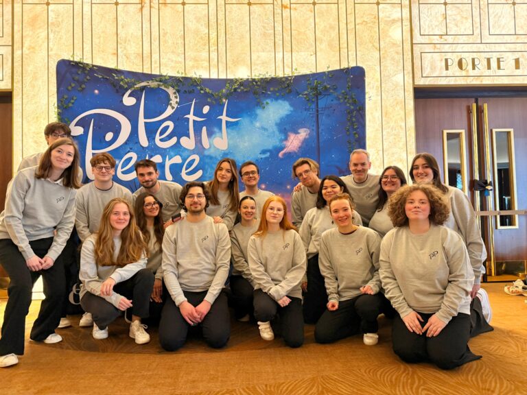 Les choristes du chœur Ineffable en sweat gris posant devant le décor du spectacle « Petit Pierre » au Grand Rex