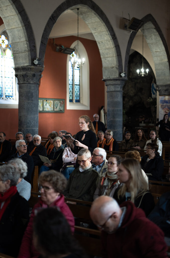 Une choriste lit un texte devant le public assis, à l'église de Chéreng, lors du concert partagé avec l'ensemble vocal Résonance.