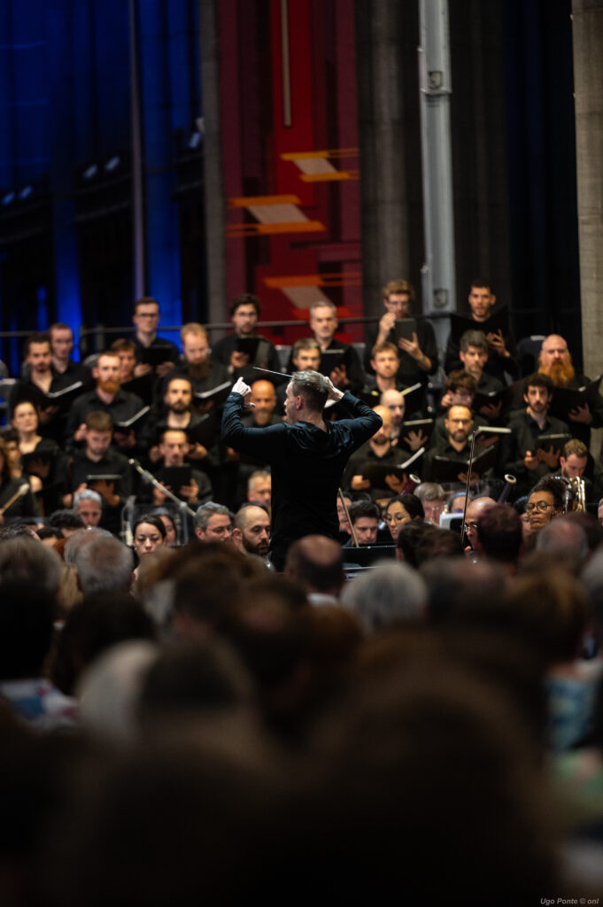 Paweł Kapuła dirigeant le Te Deum, vu depuis le public Paweł Kapuła de dos dirigeant le chœur et l'orchestre, vu depuis le public